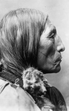 an old black and white photo of a native american man with feathers on his head