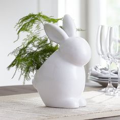 a white bunny figurine sitting on top of a table next to wine glasses