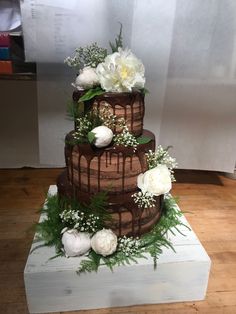 a three tiered cake with white flowers and greenery on the top is sitting on a wooden table