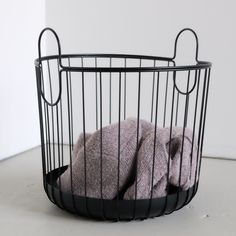 a black wire basket filled with blankets on top of a white table next to a wall