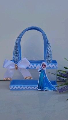 a blue purse with a white ribbon and a frozen princess figure on the front, sitting next to lavender flowers