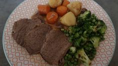 a white plate topped with meat, vegetables and potatoes next to broccoli on a table