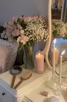 a dresser with flowers and candles on top of it next to a mirror that is reflecting the room's light