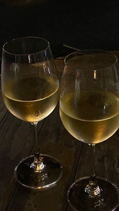 two glasses of white wine sitting on top of a wooden table next to each other