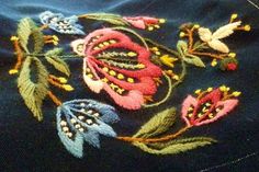 an embroidered piece of cloth with flowers and leaves on the side, sitting on a table