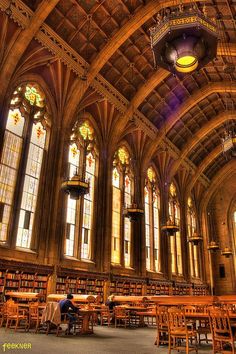 the interior of a large library with many tables and chairs in front of two tall windows