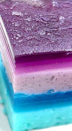 three layers of cake with blue, purple and green frosting on them sitting on top of each other