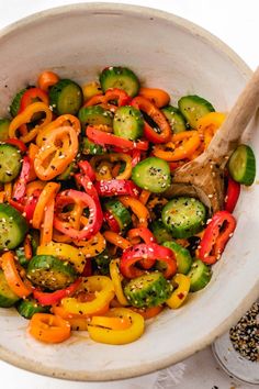 a white bowl filled with mixed vegetables on top of a table next to a wooden spoon