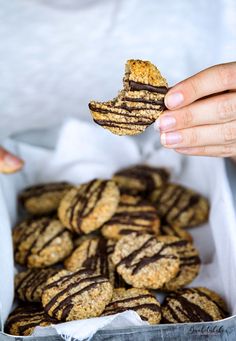 a person holding a cookie in front of a box of cookies with chocolate drizzled on them