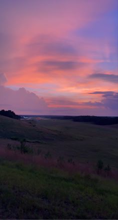 the sky is purple and pink as the sun sets in the distance over an open field