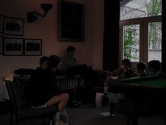 several people sitting in a living room watching television and playing pool on a green table