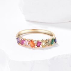 a yellow gold ring with multicolored stones on the side, sitting on a white surface