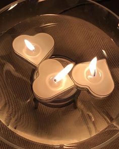 three white candles in a glass bowl on a table with two hearts cut out of them