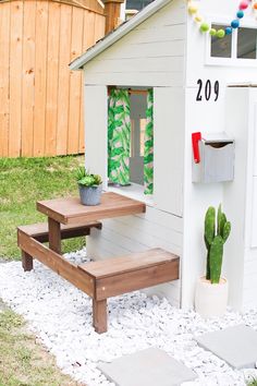 there is a small house with a table and bench in front of the door, next to a cacti