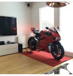 a red motorcycle sitting on top of a wooden floor next to a flat screen tv