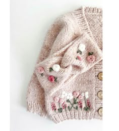 a knitted sweater with flowers and buttons on the front, sitting on a white surface