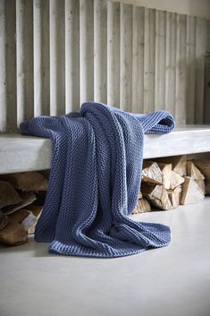 a blue blanket sitting on top of a wooden bench next to firewood stacked in front of it