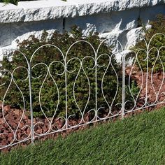 a white iron fence sitting next to a lush green field