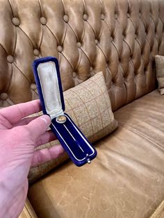 a person holding an open ring box in front of a brown leather couch with pillows