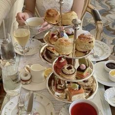 a woman sitting at a table filled with plates and cups full of tea, pastries and desserts