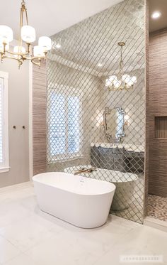 a bathroom with a bathtub, chandelier and mirror on the wall above it