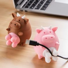 two little pigs plugged in to a computer charger on a wooden table next to a laptop