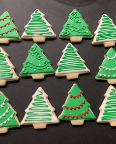 twelve decorated christmas tree cookies arranged in rows on a black surface with white icing