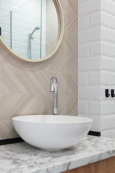 a white bowl sink sitting on top of a marble counter next to a round mirror