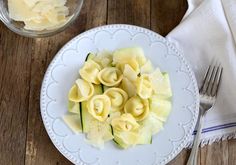 a white plate topped with ravioli and cucumbers next to a glass of water