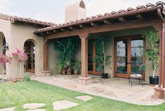 a patio with chairs and potted plants on the side of it in front of a house