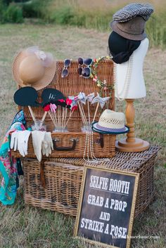 a wicker picnic basket with hats, sunglasses and props on display in the grass next to a sign that says selte booth grab a prop and strike a pose