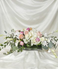 a vase filled with lots of flowers on top of a white cloth covered tablecloth