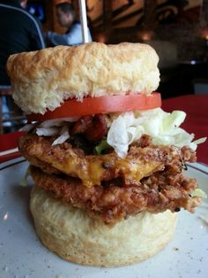 a sandwich with meat, cheese and tomatoes on it sitting on top of a biscuit