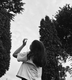 a woman flying a kite in the air next to some trees and bushes on a cloudy day