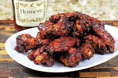 a white plate topped with chicken wings next to a bottle of hennesy barbecue sauce