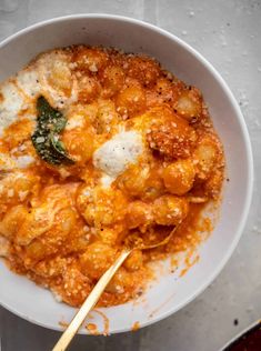 a white bowl filled with pasta and cheese on top of a table next to a wooden spoon