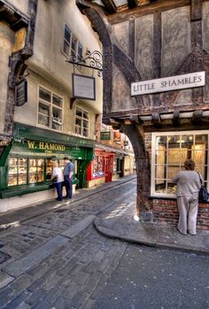 two people are walking down the street in front of some shops and stores that have little shambles on them