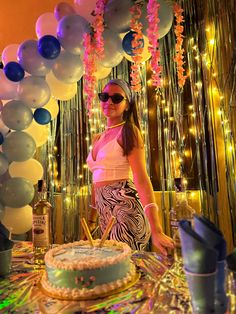 a woman standing in front of a cake and balloons