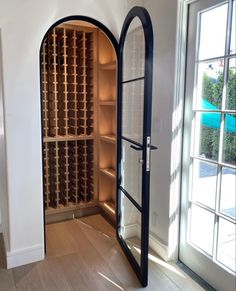 an arched wine rack in the corner of a room with windows and wood flooring