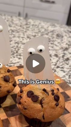 two chocolate chip muffins sitting on top of a wooden cutting board with googly eyes