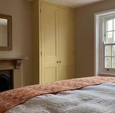 a bed with an orange comforter sitting in front of a window next to a fireplace