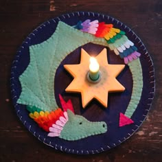 a lit candle is placed on top of a small plate with colorful fabric pieces around it