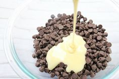 chocolate chips and cream being poured into a glass bowl with melted butter on top,