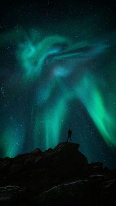 a person standing on top of a hill under the stars and green lights in the sky