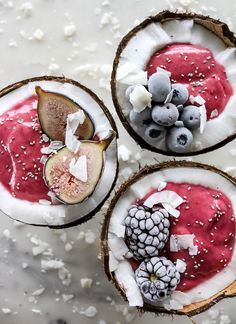 three coconuts with fruit and yogurt in them on a white table top