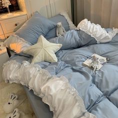 a bed with blue sheets and white ruffles is shown in this image, there are two stuffed animals on the pillow