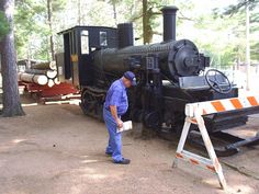 a man standing next to an old fashioned train in the middle of a wooded area