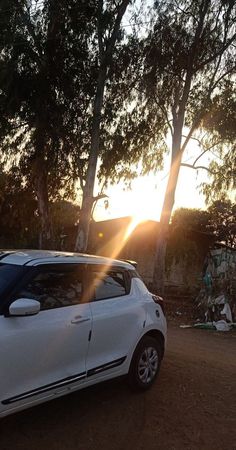 a white car parked on the side of a dirt road next to trees and tents