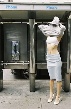 a woman in a skirt and hat standing next to a phone booth on the sidewalk