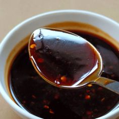 a spoon full of sauce sitting in a white bowl on top of a wooden table